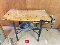 Front view of bench showing metal top, steel legs, attached stool, vise, bench dog holes