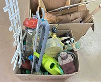 Box containing assorted garden items including watering can, lantern, trellis, stakes and small parts