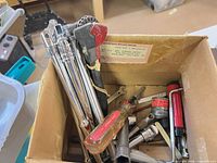 Box of mixed hand tools showing socket extensions, adjustable wrench, screwdrivers