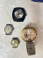 Group shot of four wristwatches on light surface