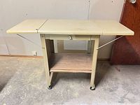 Full view of table with both leaves raised, showing drawer, shelf and casters