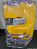 Front view of sealed package showing three nested yellow cutting boards with purple edges
