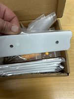 Open box showing stack of white brackets and hardware bags