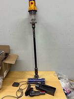 Full view Dyson stick vacuum assembled with attachments nearby