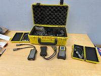 Lot overview showing yellow case open, handheld units, cables, accessory cases