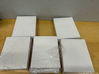 Five shrink-wrapped packs of white cardstock on table