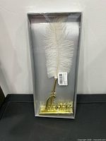 Sealed box showing white feather pen and gold LOVE base