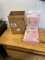 Two sealed bags of Beans Royale Tofu Cat Litter next to shipping box