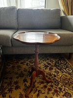 Scalloped round top wooden pedestal side table with tripod base