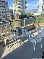 Bistro table with two white patio chairs, ceramic planter and small lidded jar on balcony