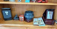 Shelf view showing all items: figurine, stone urn, red lacquer box, prints, vanity box