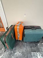 Three suitcases lined up: green fabric, orange hard, teal hard