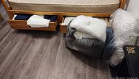 Drawer under bed with folded linens and vacuum-sealed bedding on floor