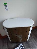 Hamper top and perforated metal interior with handles visible