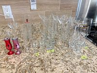 Group view of assorted clear glass stemware, champagne flutes, shot glasses, Stella Artois pilsners, San Miguel beer boot, NCL metal shooters