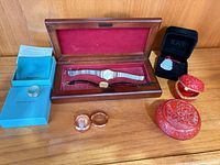 Overview of all items including watch in wood case, IDee box with pendant, two cinnabar boxes, two rings, Tiffany packaging