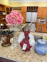 Group shot showing black ceramic vase, red glass vase, clear glass bud vase with pink faux hydrangeas inserted, and blue-white lidded jar