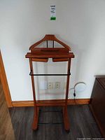 Front view of wood valet stand showing hanger, tray, pants bar, casters