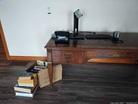 Desk area showing monitor base, HP keyboard, tray with staplers, and stack of books