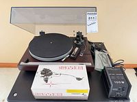 Turntable with dust cover open, SME tonearm box, AC adaptor, cables visible
