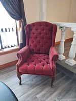 Front view of burgundy tufted wingback chair showing upholstery, tufting, nailhead trim and legs