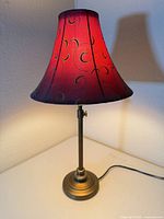 Full view of lamp lit showing metal base and red embroidered shade
