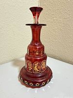 Full view of cranberry decanter with stopper inserted showing gilt floral panels and base ring pattern