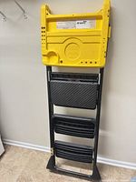 Front view of folded Cosco 3-step ladder showing yellow top and black steps