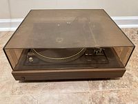 Turntable with dust cover closed showing walnut plinth and smoked lid