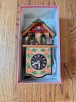 Entire cuckoo clock in box showing painted chalet design and dial