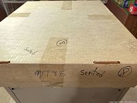 Closed cardboard five-row storage box with handwritten notes on lid