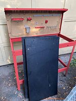 Full view of red metal workbench with pegboard and black panels leaning against it