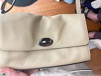 Front of beige leather crossbody showing turn-lock and leather texture