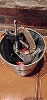 Bucket filled with assorted clamps, shows quantity, materials and condition.