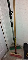 Overall view of both long-handle deck brushes standing against wall