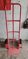 Full view of red steel hand truck showing frame, toe plate and pneumatic wheels