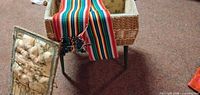 Wicker sewing box on metal legs, lid removed, striped sash draped over side