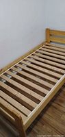 Angled view of natural pine twin bed frame showing complete frame and slatted base
