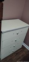 Full view of off-white painted four-drawer dresser showing ceramic knobs and decorative top edge