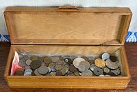 Wooden box open showing contents of assorted coins and one banknote