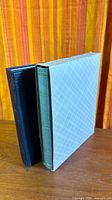 Green stockbook inside patterned slipcase beside black binder
