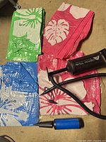 Four folded vinyl floaties in blue, green, and pink prints with black AquaTRAX pump and blue pump displayed on floor