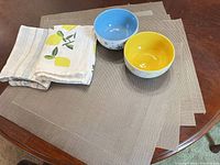 Lot showing six taupe placemats, two tea towels and two patterned ceramic bowls on a wooden table