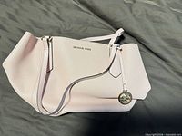 Full exterior view of light pink Michael Kors tote with straps and hanging medallion