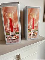 Two boxed silver-plated hurricane lamp sets displayed side by side