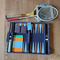 Open backgammon case showing pieces, dice, paperwork; tennis and badminton racquets