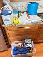 Overall view of countertop items: Igloo cooler, jerry can, small first-aid bin, travel mug, disposable cups, utensils, plastic wrap