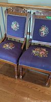 Front view of both chairs showing carved backs, floral needlepoint panels, turned legs