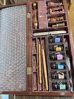 Open wooden calligraphy case showing pens, nibs, ink jars, seal tools
