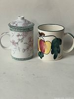 Blossom lidded mug beside apple motif mug front view